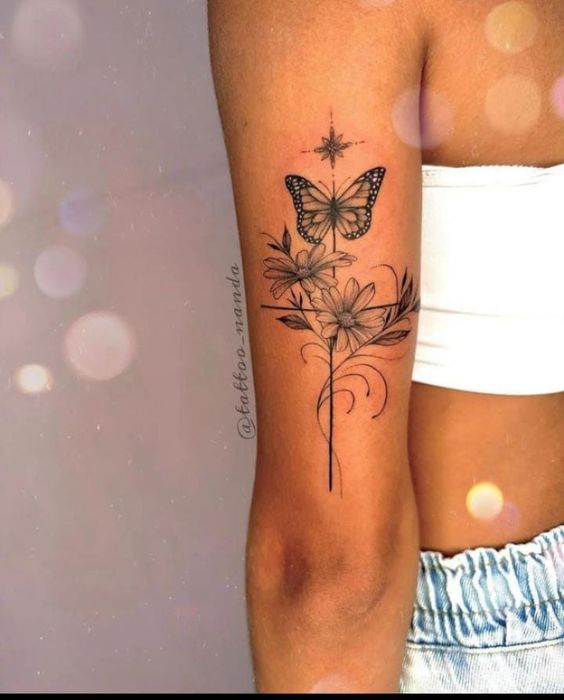 Bra&ccedil;o com tatuagem de borboleta e flores em estilo delicado, fundo desfocado com efeito de luzes circulares.