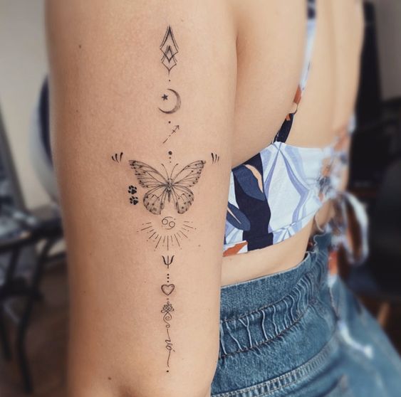 Tatuagem no bra&ccedil;o com borboleta, s&iacute;mbolos geom&eacute;tricos e astrol&oacute;gicos, em design delicado e linear.