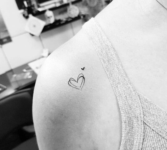 Pessoa com tatuagem de cora&ccedil;&atilde;o e s&iacute;mbolo pequeno no ombro, vestindo uma blusa de al&ccedil;as finas.