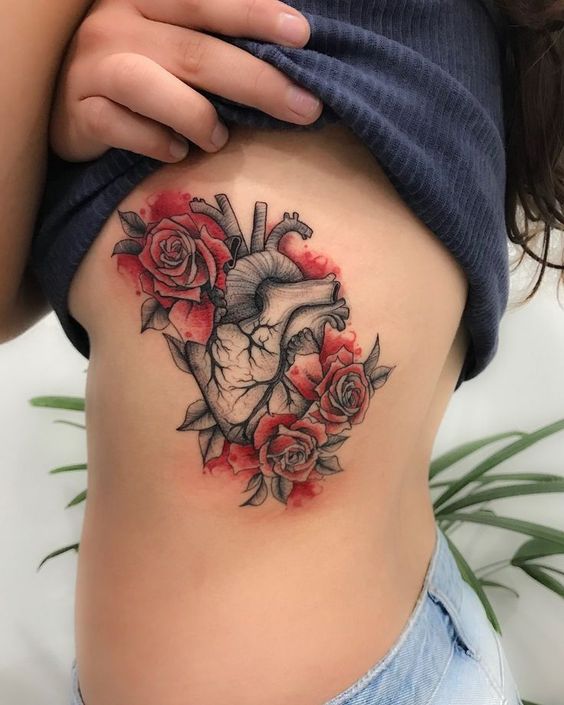 Tatuagem de coração anatômico com rosas e detalhes vermelhos na lateral do corpo.
