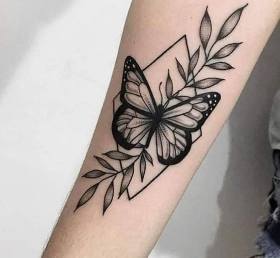 tatuagem-de-borboleta-com-flores-3 Tatuagem de borboleta preta com folhas e formas geométricas no braço de uma pessoa.