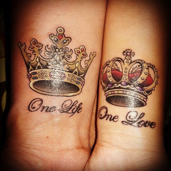 Duas tatuagens de coroas nos pulsos, uma com a frase "One Life" e a outra com "One Love".