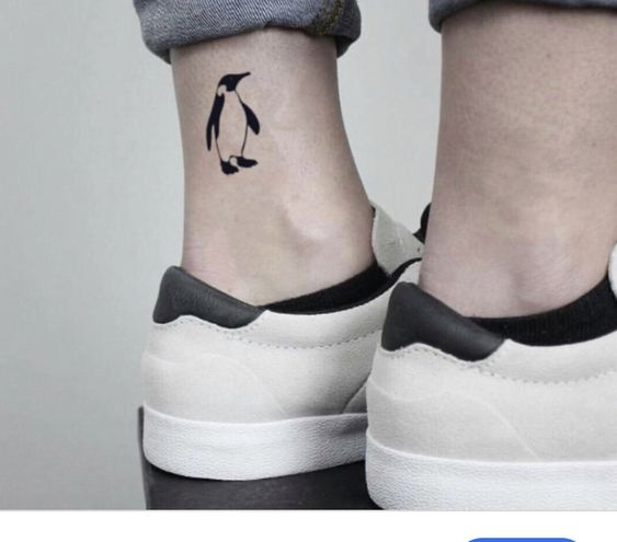 Pessoa com tatuagem de pinguim no tornozelo, usando tênis claros e calça jeans dobrada.