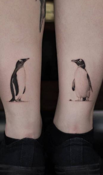 Duas tatuagens de pinguins estão localizadas nas pernas de uma pessoa, próximas aos tornozelos.