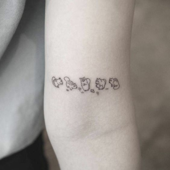 Uma tatuagem minimalista no bra&ccedil;o mostra cinco gatos estilizados em diferentes posi&ccedil;&otilde;es.
