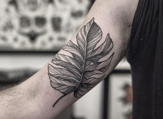 Braço com tatuagem detalhada de folha em estilo preto e cinza.