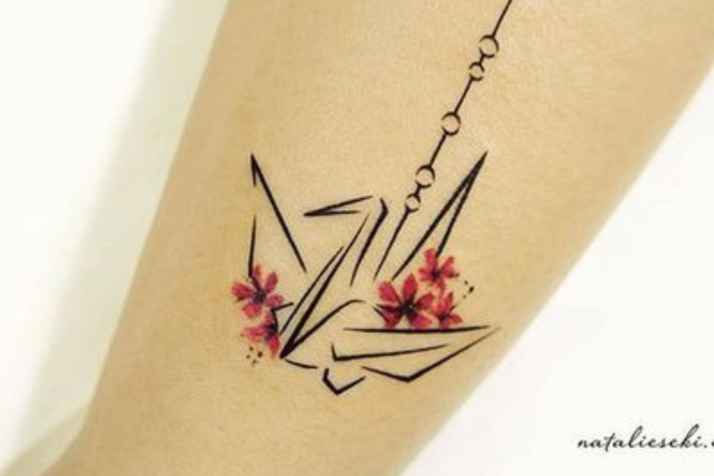 Tatuagem de origami de p&aacute;ssaro com flores vermelhas e detalhes geom&eacute;tricos no bra&ccedil;o.