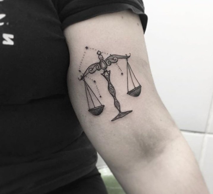 tatuagem-balanca-4 Braço com tatuagem de balança estilizada e constelação em fundo claro.