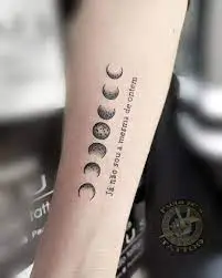 Uma tatuagem no bra&ccedil;o com fases da lua e texto ao lado.