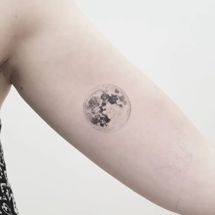 Bra&ccedil;o com uma tatuagem de lua em preto e branco, sobre fundo branco.