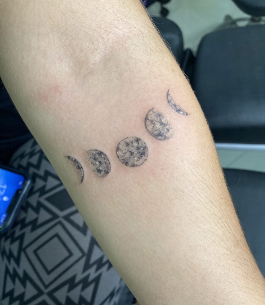 Tatuagem de fases da lua no bra&ccedil;o de uma pessoa, com cinco etapas distintas da lua.