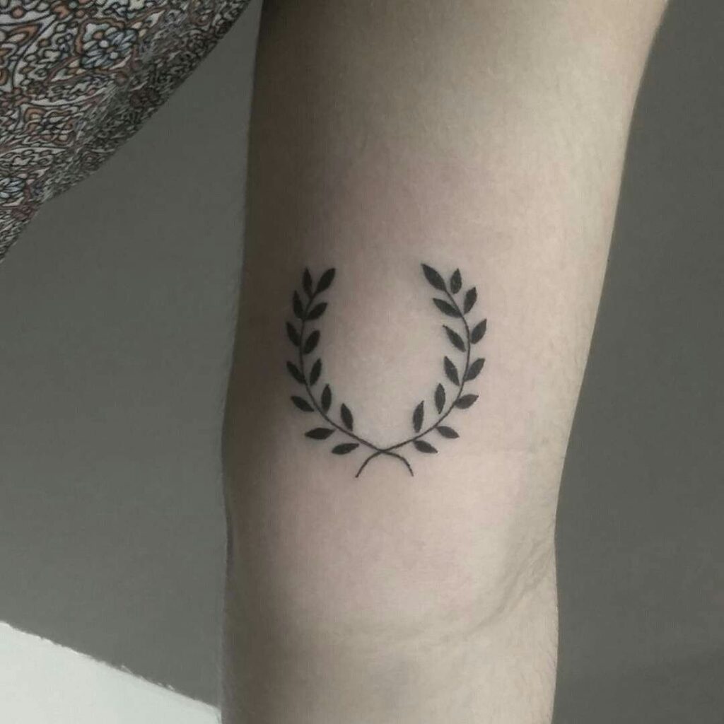 Tatuagem de coroa de louros preta no braço, símbolo de vitória e honra. Design minimalista e elegante.