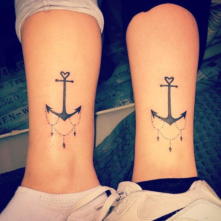 Duas pernas com tatuagens id&ecirc;nticas de &acirc;ncoras estilizadas, com cora&ccedil;&otilde;es e detalhes pontilhados.