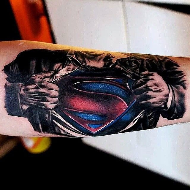 tatuagem-superman-2 Tatuagem no braço de personagem rasgando camisa, revelando símbolo vermelho e azul no peito.