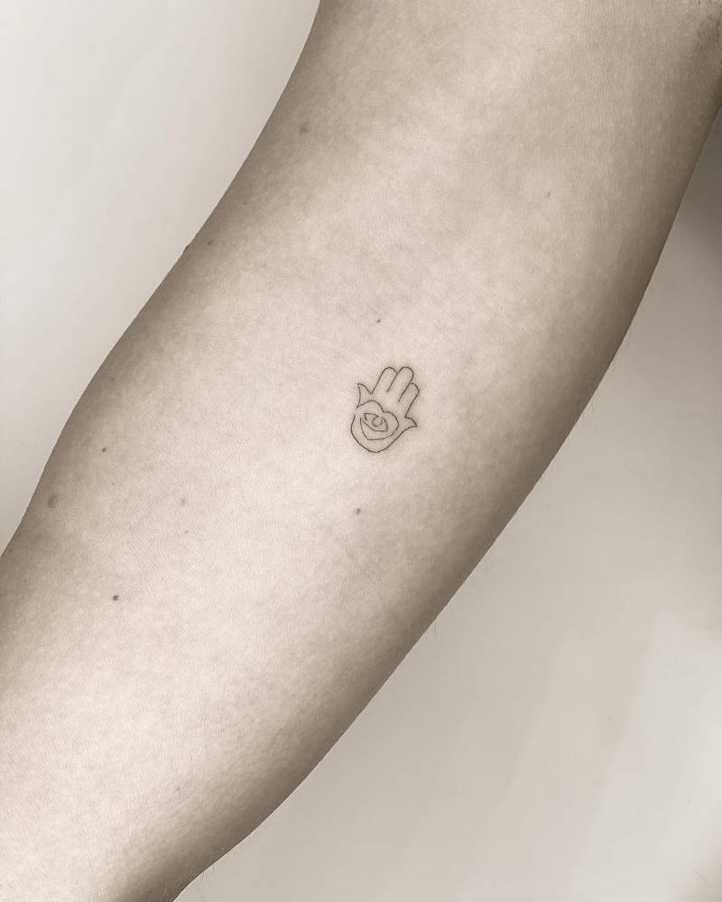 Bra&ccedil;o com pequena tatuagem de m&atilde;o com um olho no centro. Fundo neutro.