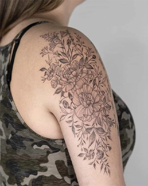 Pessoa com uma tatuagem de flores detalhadas no ombro, usando uma blusa camuflada.
