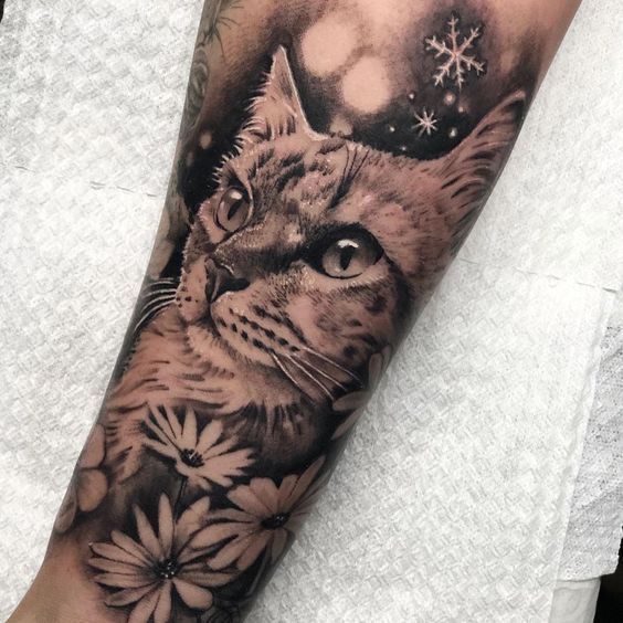 tatuagem-de-gato-2 Tatuagem de gato com flores e flocos de neve em um braço.