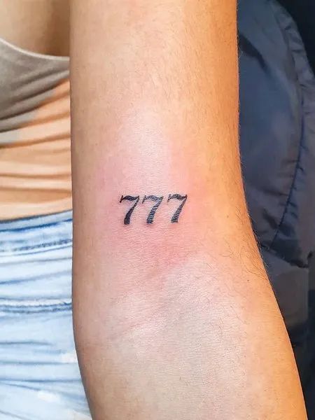 tatuagem-777-2 Braço com uma tatuagem do número "777" em tinta preta.