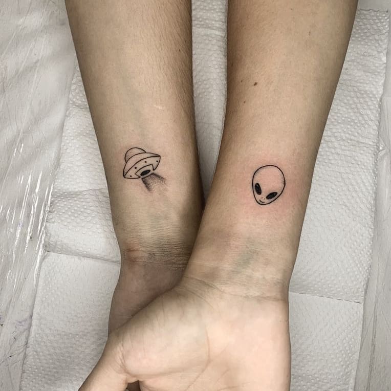 tatuagem-de-et-29 Dois braços com tatuagens minimalistas, uma de disco voador e outra de rosto de alienígena.