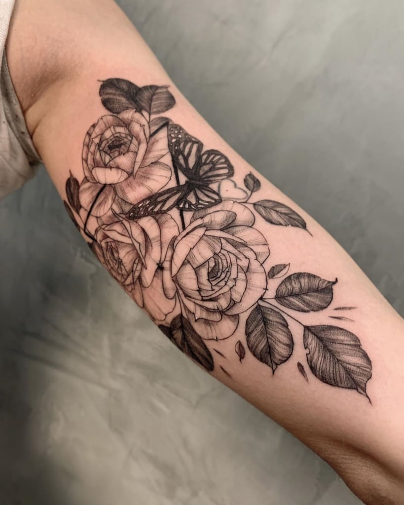 w819-7 Braço com tatuagem de rosas e borboleta em tons de preto e cinza, detalhadamente desenhadas.