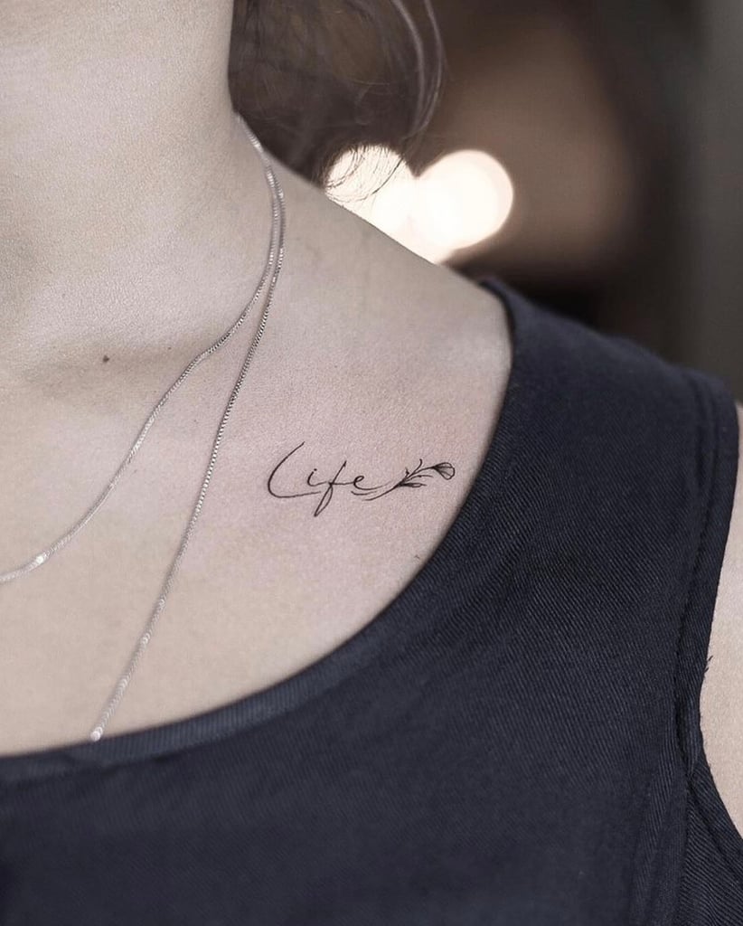 w822-3 Pessoa usando colar prateado e camiseta preta com tatuagem "Life" no ombro.