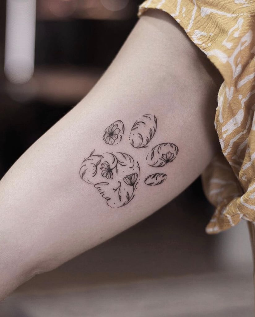 w824 Uma tatuagem de pegada com detalhes florais no braço de uma pessoa.