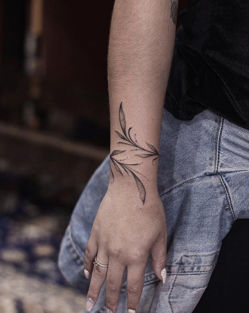 w814 Mão com anéis e unhas claras, tatuagem de folhas no antebraço, jaqueta jeans amarrada na cintura.