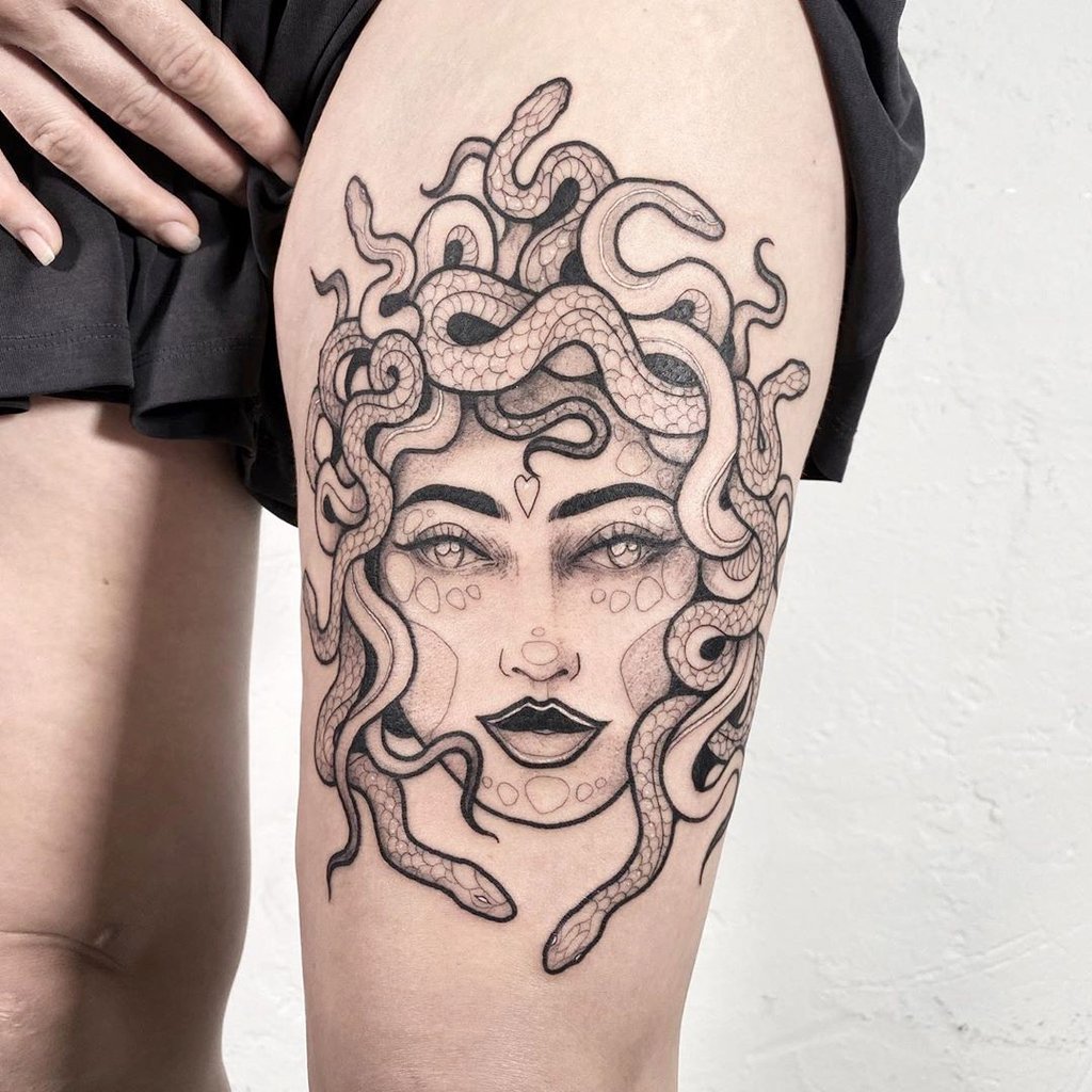 Tatuagem detalhada de Medusa no estilo line work preto e cinza na coxa feminina, com serpentes entrelaçadas no cabelo.