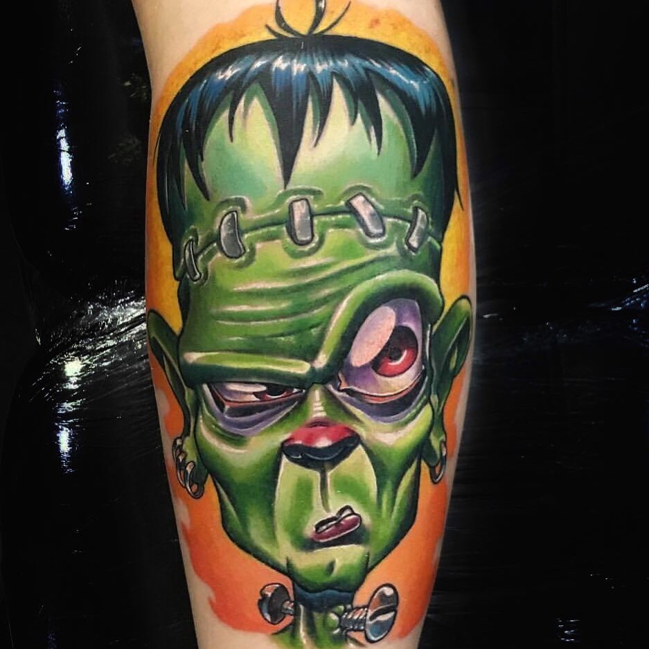 19xgpzec3fugigp8cfwljlg-1 Tatuagem colorida de criatura verde com expressão séria, cabelo escuro e parafusos no pescoço, em fundo laranja.