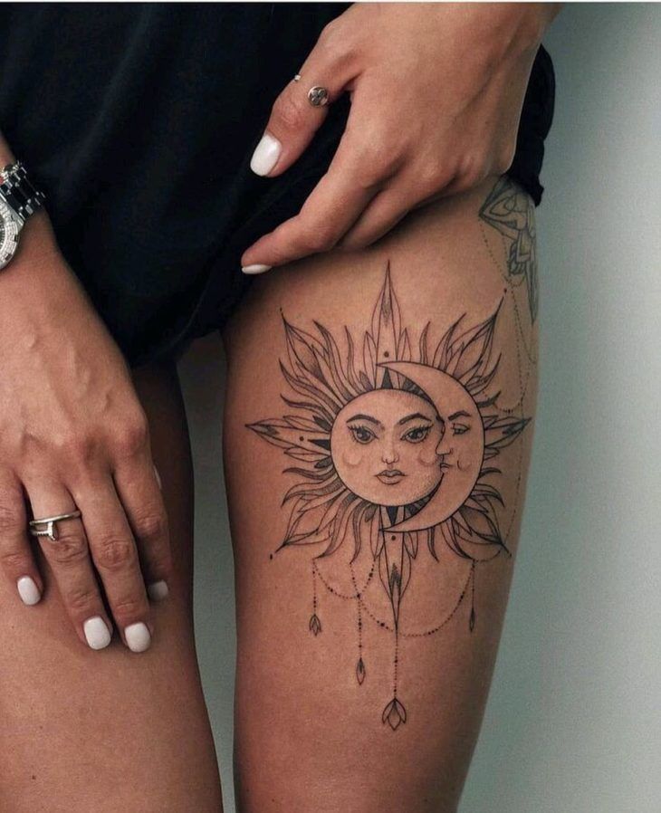 7966cab4d907f02fe9ec97581d7b3a1f Tatuagem de sol e lua com rostos em perna, adornada com detalhes pendentes. Mão com anéis ao lado.