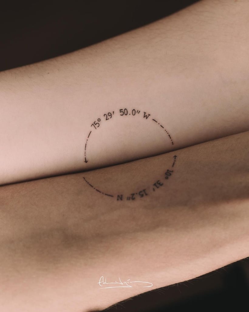 Duas pessoas com tatuagem de coordenadas geográficas em forma de arco nos braços, indicando localização específica.