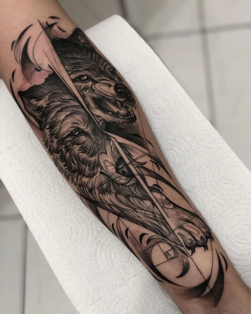 Tatuagem de lobo estilizado em preto e cinza no braço, com detalhes geométricos e sombreados.