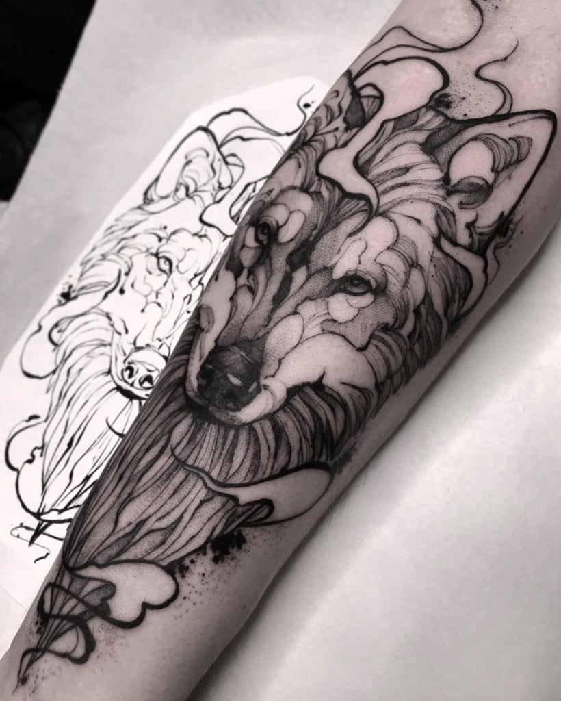Braço com tatuagem de lobo detalhada, ao lado de desenho em papel com o mesmo tema.