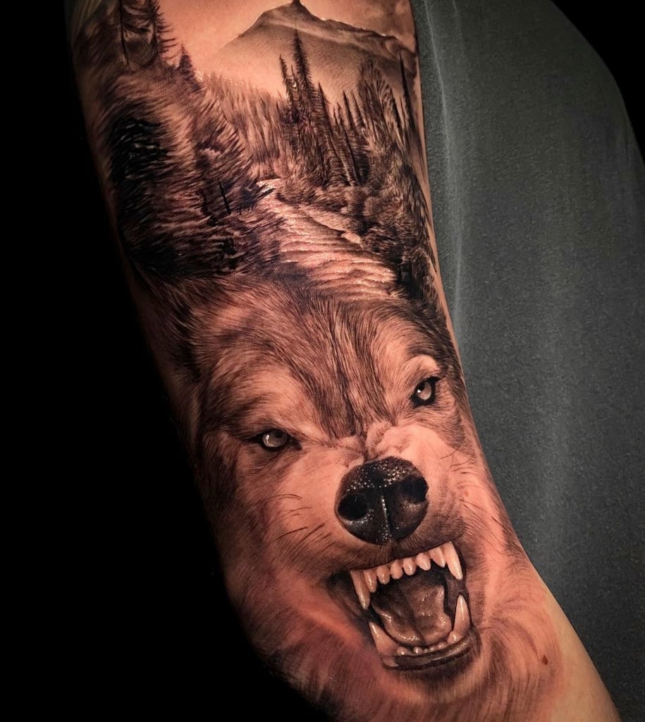 Tattoo detalhada de lobo com paisagem florestal no braço de uma pessoa, exibindo realismo impressionante.