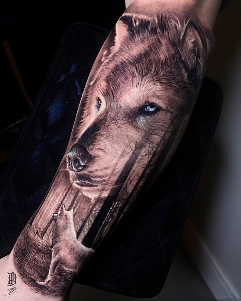 Tatuagem realista de lobo com olhos azuis, em um braço, destacando detalhes do pelo e olhar intenso.