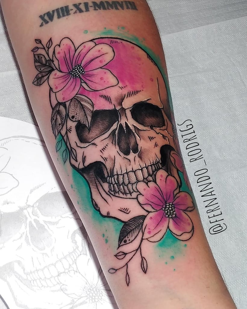 w820-32 Desenho de crânio com flores rosa e folhas em um braço tatuado.