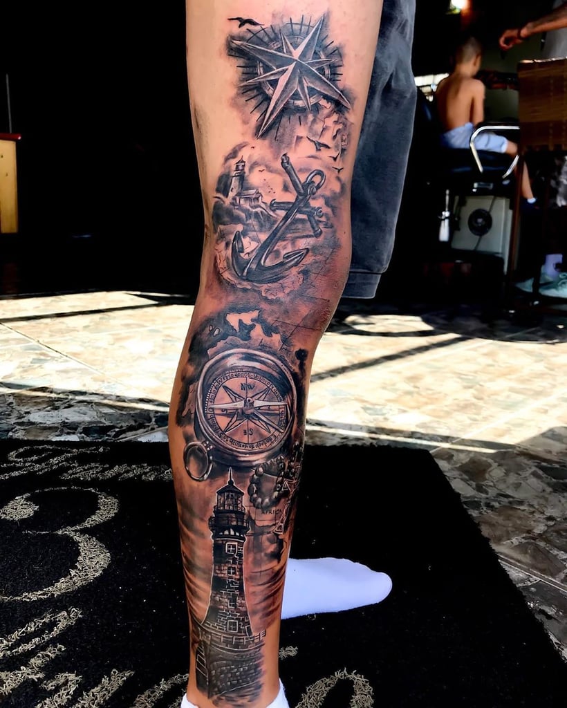 w820-33 Perna tatuada com rosa dos ventos, âncora, bússola e farol, em ambiente interno.