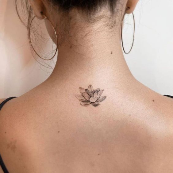 Tatuagem delicada de flor lotu no pescoço, evidenciando estilo e elegância feminina; cabelo preso e argolas grandes completam o visual.
