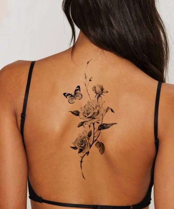 Mulher com tatuagem nas costas de rosas e borboleta, usando lingerie preta. Desenho delicado e elegante.