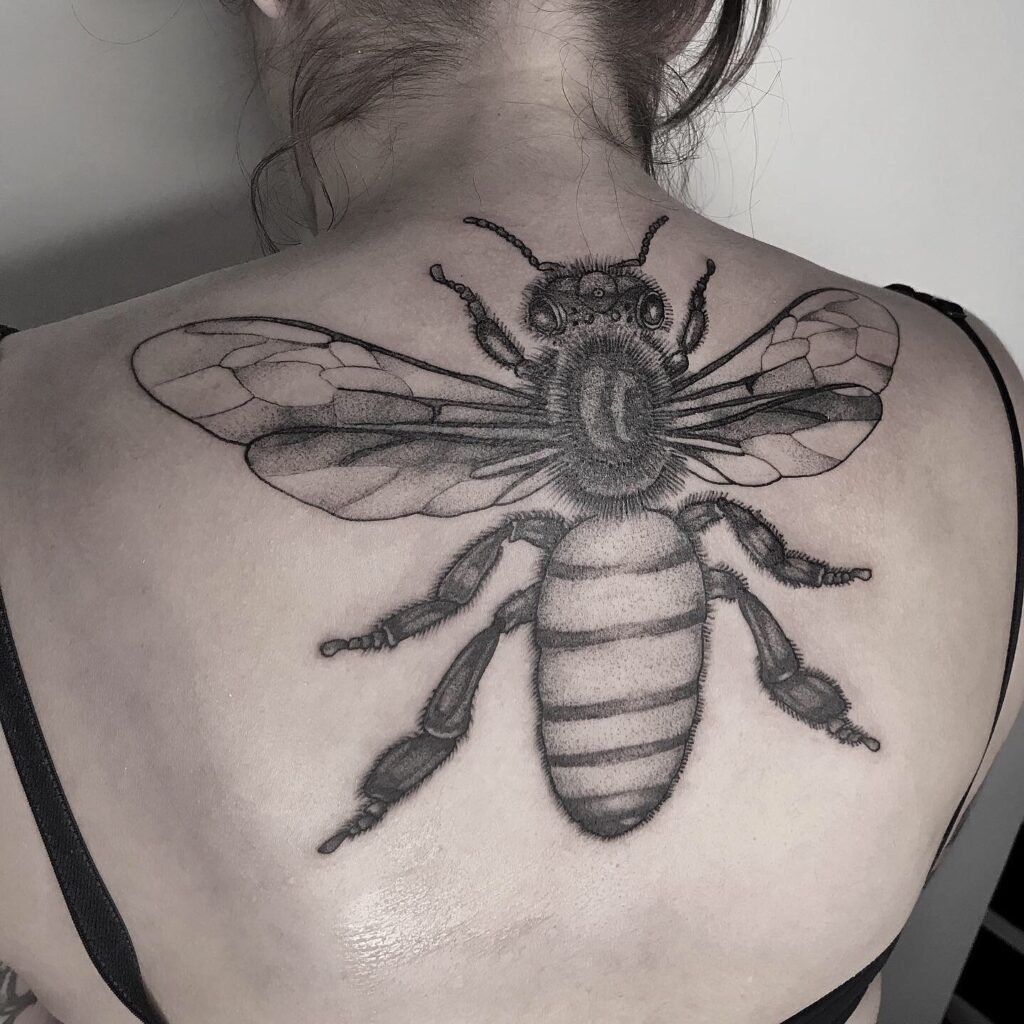 Tatuagem de abelha detalhada nas costas de mulher, exibindo design artístico e precisão no traço.