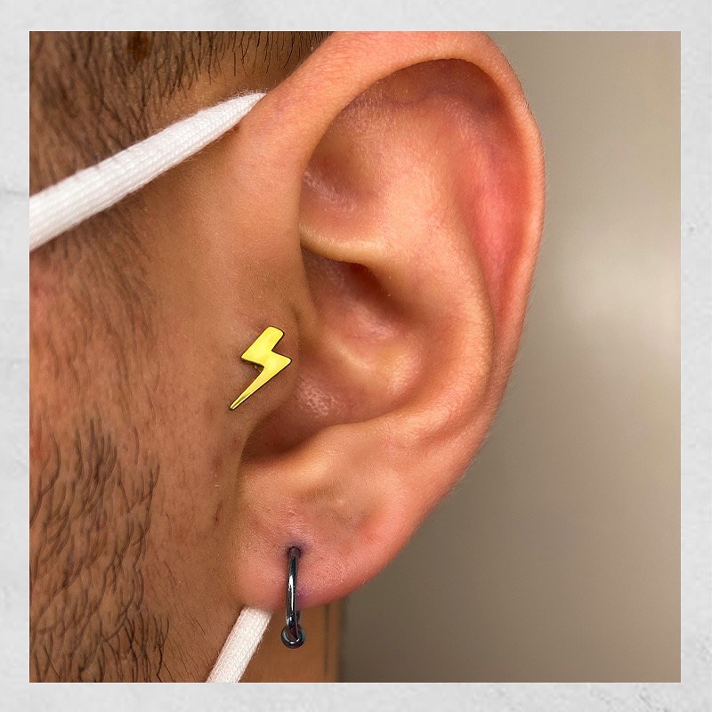 Orelha com piercing de raio dourado e argola preta, estilo moderno e fashion.