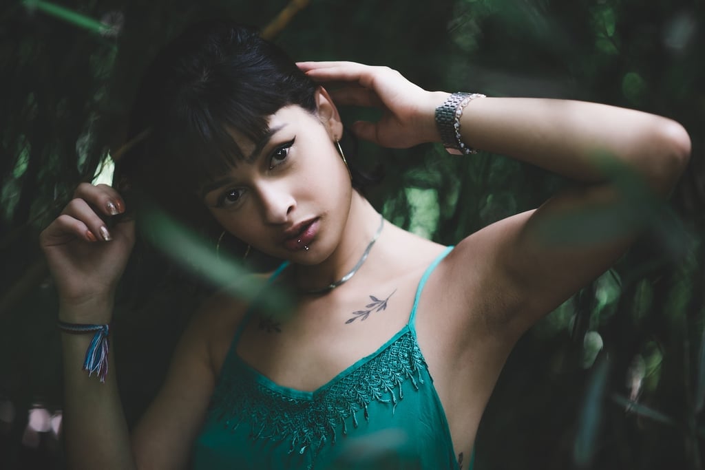 Mulher de vestido verde em meio a folhagens, olhando para a câmera. Estilo boêmio e natural.