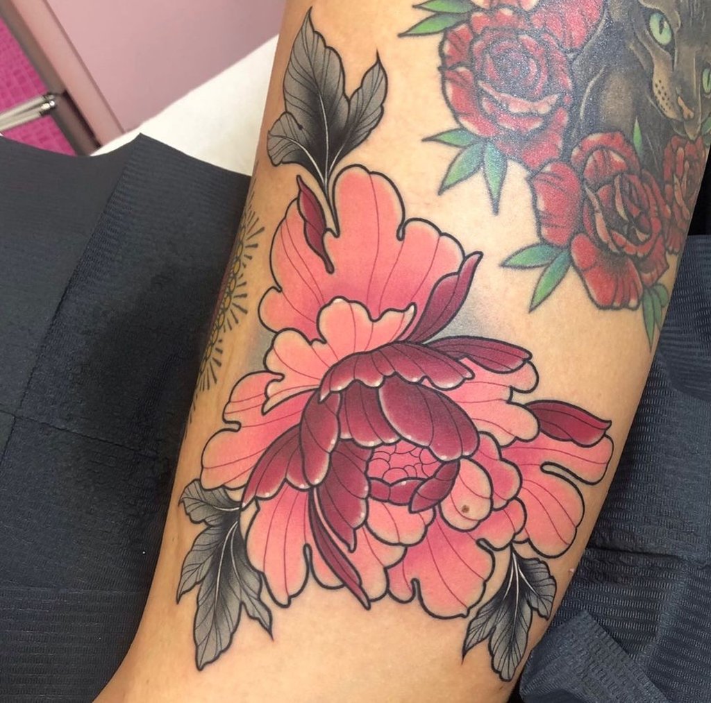 Tatuagem de flor cor-de-rosa com folhas pretas em um braço, destacando arte vibrante e detalhada.