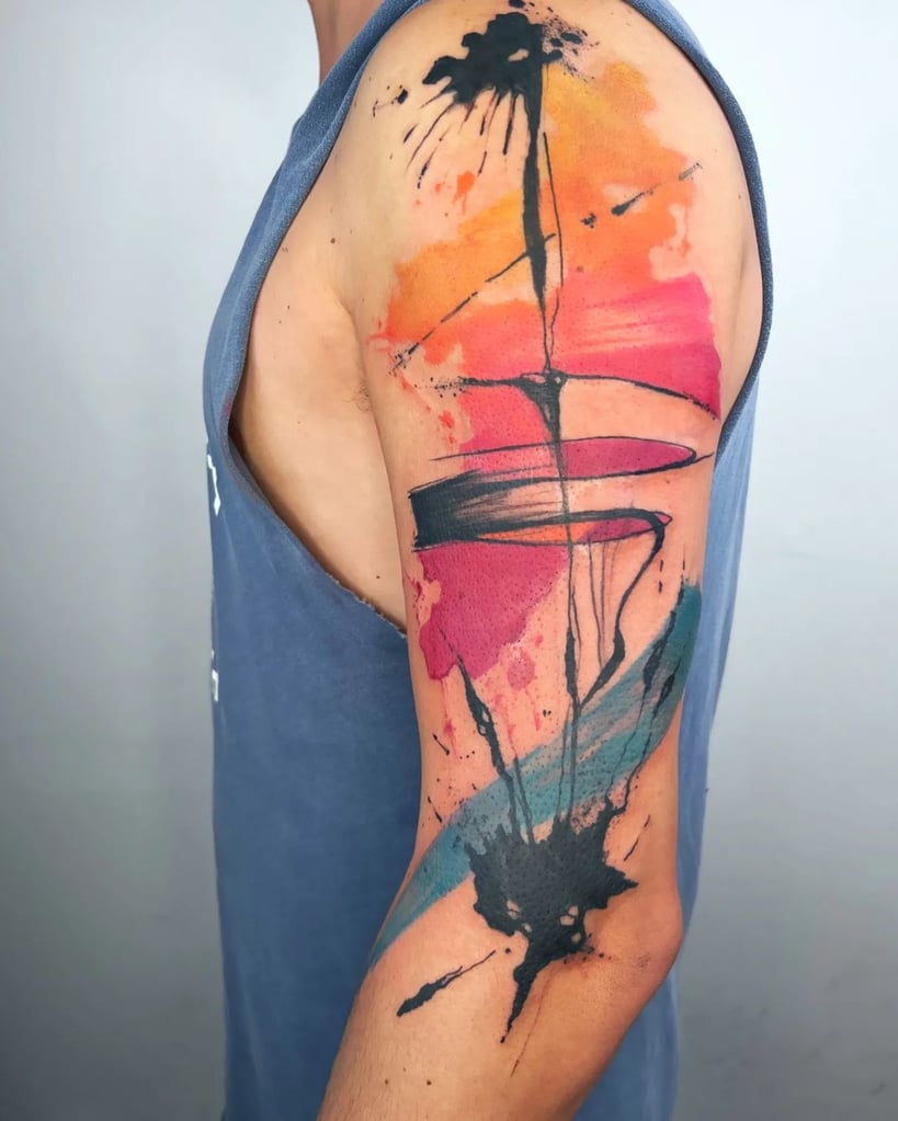 Tatuagem abstrata no braço com tinta preta e cores vibrantes como laranja, vermelho e azul, em estilo aquarela.