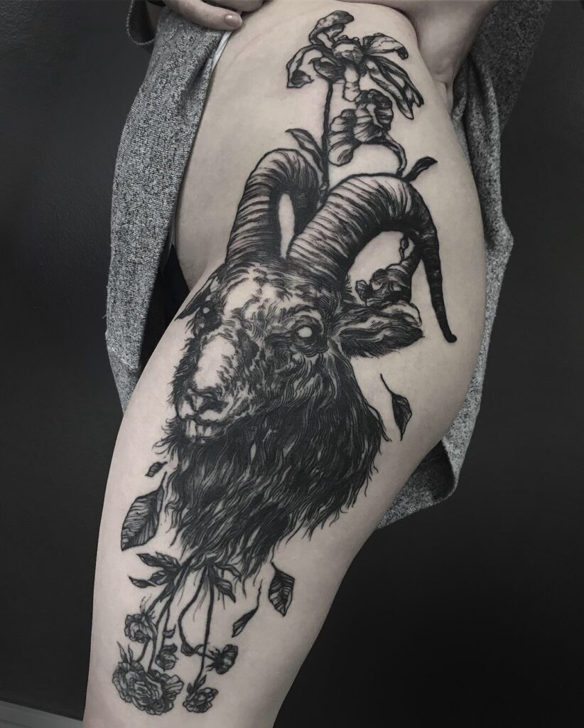 Tatuagem de bode detalhado com flores no braço, estilo realista, em pele clara, com arte sombreada em preto e cinza.