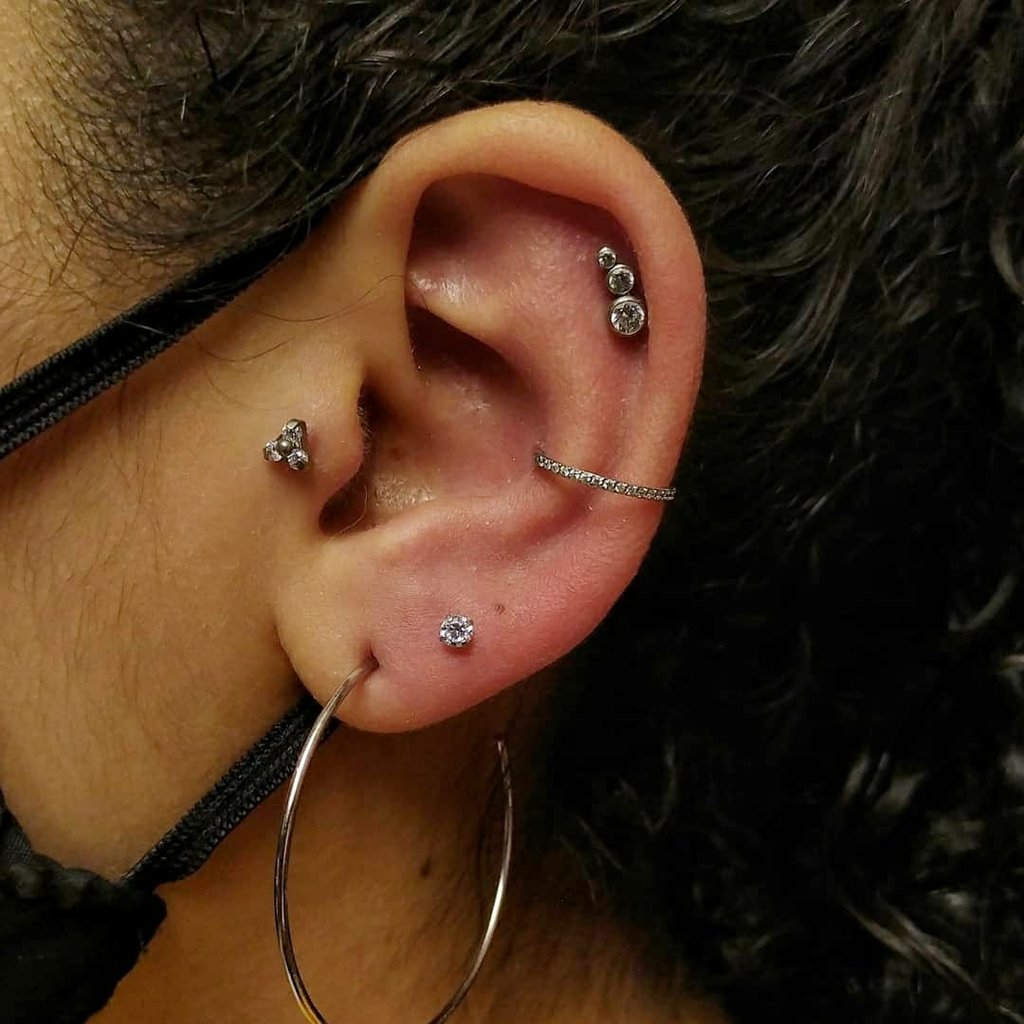 Orelha com múltiplos piercings prateados de diferentes tamanhos e formatos, destacando estilo moderno e ousado.