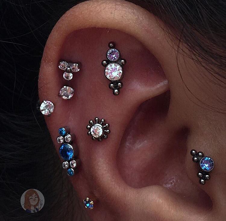 Orelha com múltiplos piercings delicados em tons de prata e azul, realçando o estilo e a personalidade.