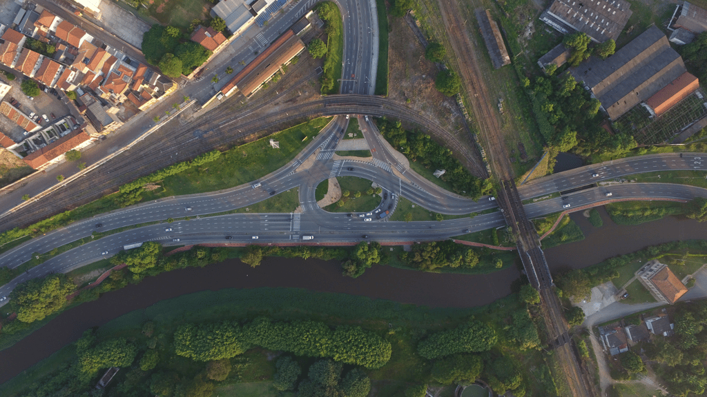 Imagem aérea de um cruzamento urbano com viadutos sobre córrego e área verde ao redor.
