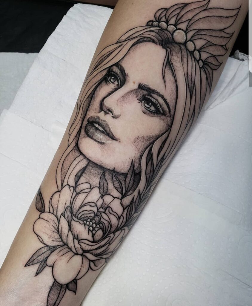 Tatuagem de rosto feminino com flores e detalhes de folhas no antebraço, estilo realista e delicado.