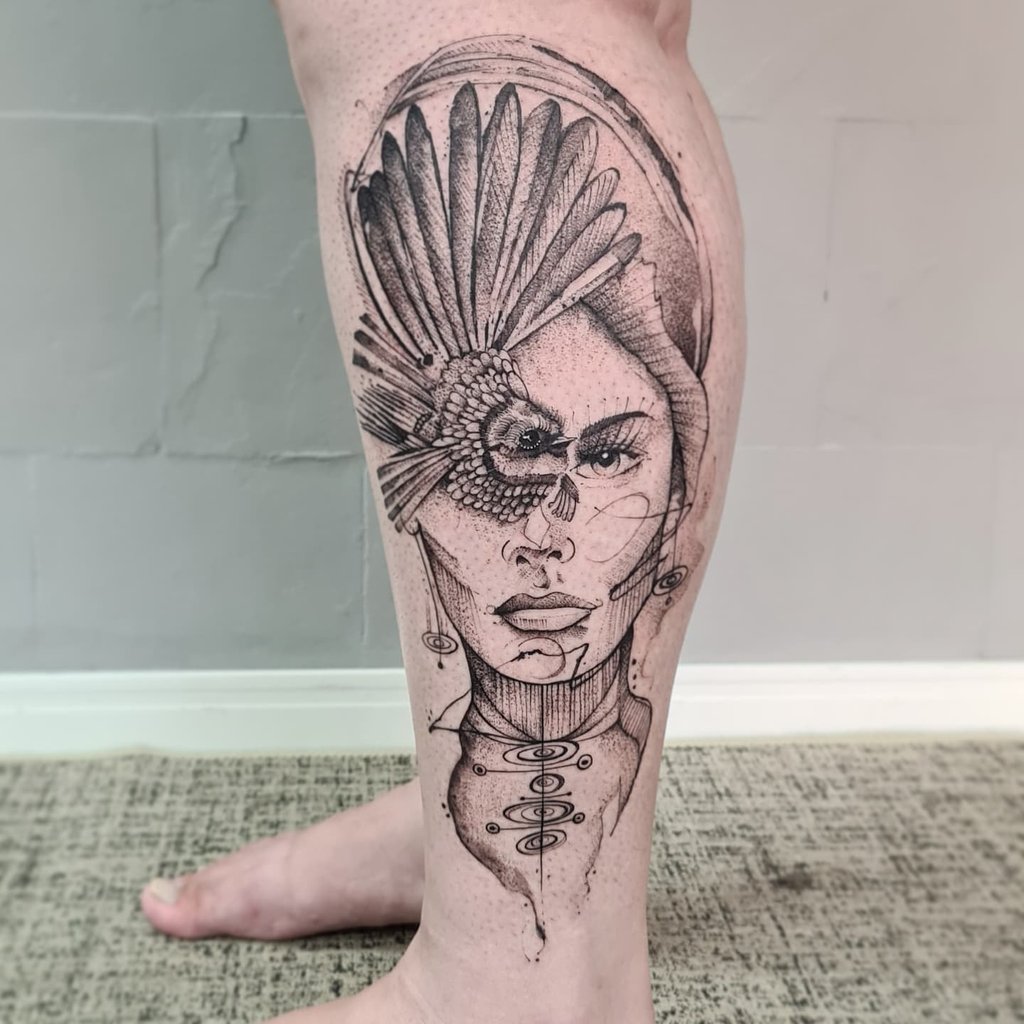 Tatuagem detalhada de rosto feminino com elementos abstratos e penas, estilo sketch, na perna.